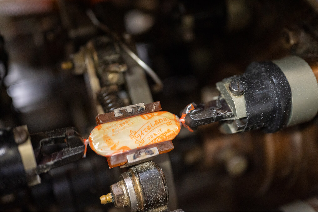 出来上がったハッピーターンを機械がキャンディータイプで包み、両端をくりっと捻る様子