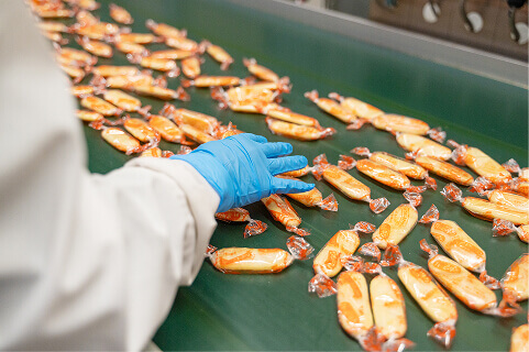 スタッフがラインを流れる個包装されたハッピーターンを品質チェックする様子